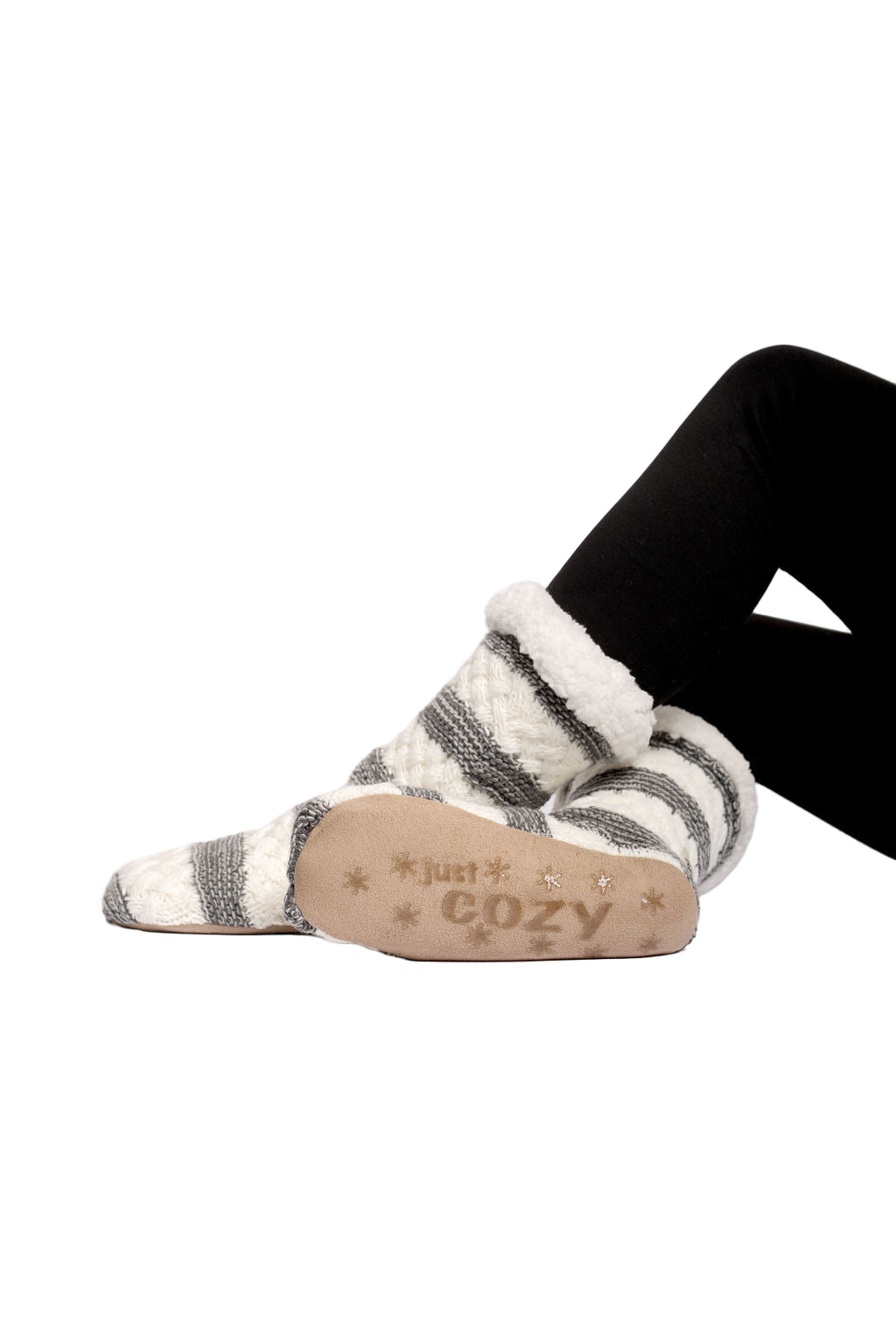 A pair of cozy slipper socks with a knitted shell and sherpa lining, featuring non-slip gripper bottoms, displayed on a person's feet.