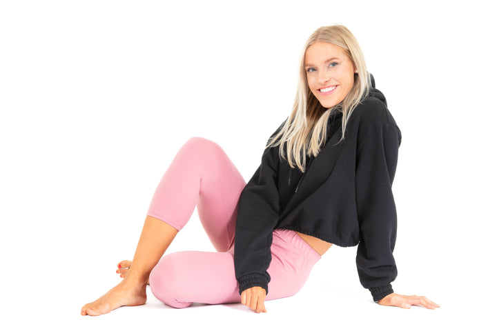 Woman wearing a black hoodie and pink leggings sitting on a white background
